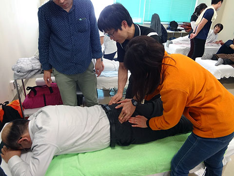 写真中央　骨盤へのアプローチを指導する山本先生