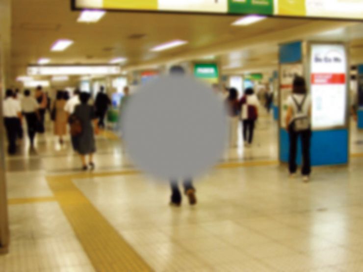 画像です。中心暗点の見え方を示しており、画像中央の駅の地下道を歩く男性の後ろ姿が灰色の円形で隠れています