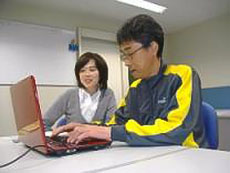 写真。パソコンの訓練に取り組む利用者と指導員。利用者がノートパソコンの入力作業をしている。