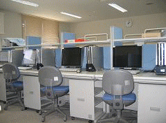 写真。室内に事務机が6台ほどあり、デスクトップパソコン、ディスプレイが各机に配置されている。