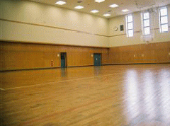 写真。体育館内部。ロッカー室、トレーニング室などがあり、可動式バスケットボール用ゴールも設置している。