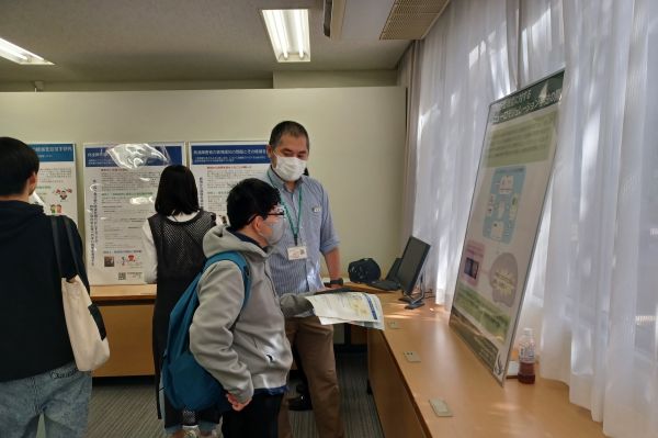 人の認知行動機能についてのパネル展示について、来場者に説明しています。