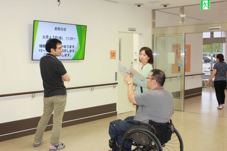 機能訓練棟 連絡用電光掲示板の前で車いす利用者や職員が掲示板を見ている写真
