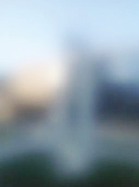 写真。弱視の見え方一例。「障害のない見え方」の写真の輪郭が非常にぼやけ、モニュメントと後ろの建物の前後を見分けられない画像。また、明るさが強く全体に白っぽく見える。