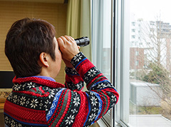 写真。利用者が教室の窓際で単眼鏡を覗いている。単眼鏡を使って、遠方の目印を見つける訓練をしているところ。