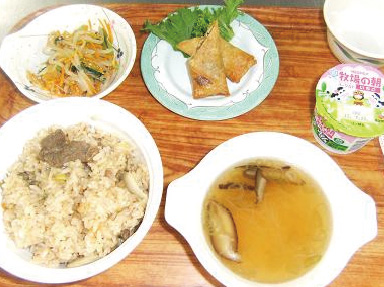写真。食事の一例。炊き込みご飯、お吸い物、モヤシのナムル、春巻き、ヨーグルト。一人分の食事をお盆に乗せて配膳。